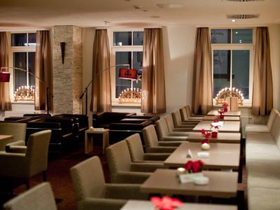 Gemütlicher Gastraum mit braunen Sesseln, langen Tischen, roten Tischdekorationen und Fensterbeleuchtung.