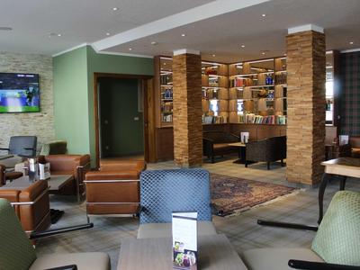 Moderner Hotel-Lounge-Bereich mit Ledersesseln, Bücherregal und hellem Parkettboden.