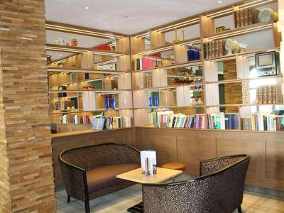 Hell eingerichteter Loungebereich mit Holzregalen, bunten Büchern, zwei Sesseln und kleinem Holztisch.