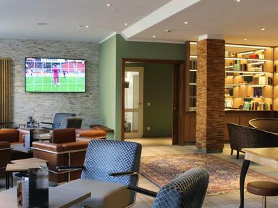 Moderner, gemütlicher Aufenthaltsraum mit Sesseln, TV an Wand, Bücherregal und warmem Licht.