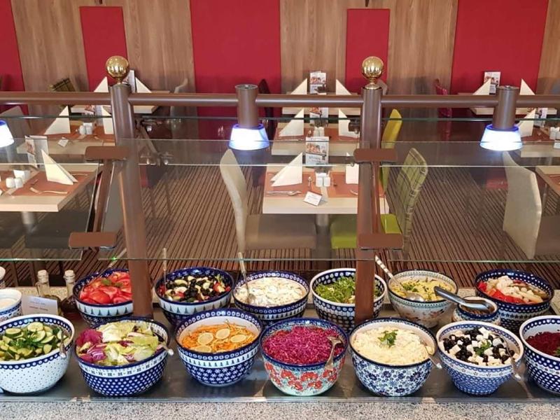 Buffet-Tisch mit bunten Schalen voller Salate und Beilagen in einem Restaurant mit roten Stühlen.