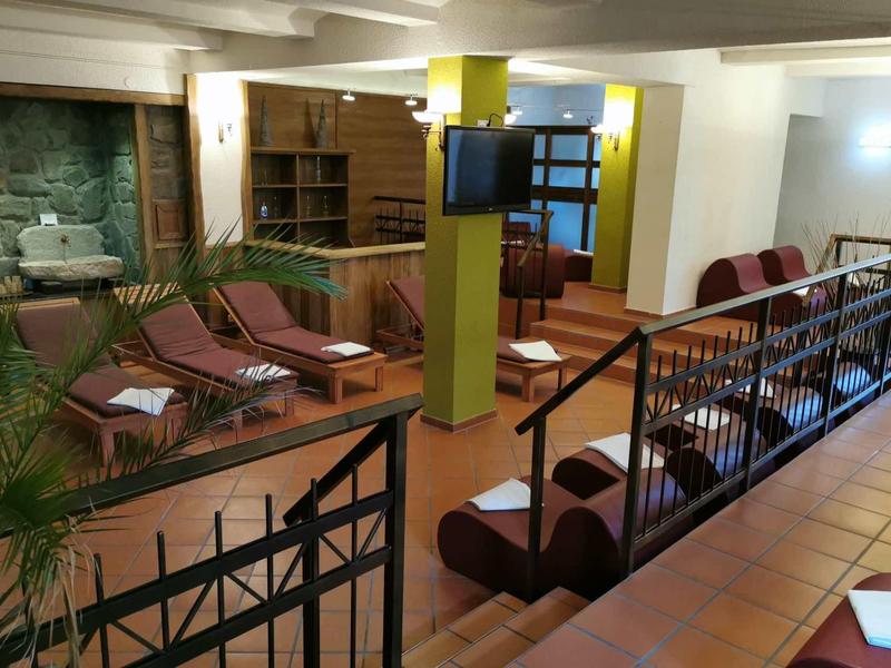 Innenraum eines Wartebereichs mit Holzmöbeln, Sesseln, gelben Säulen und Fliesenboden.