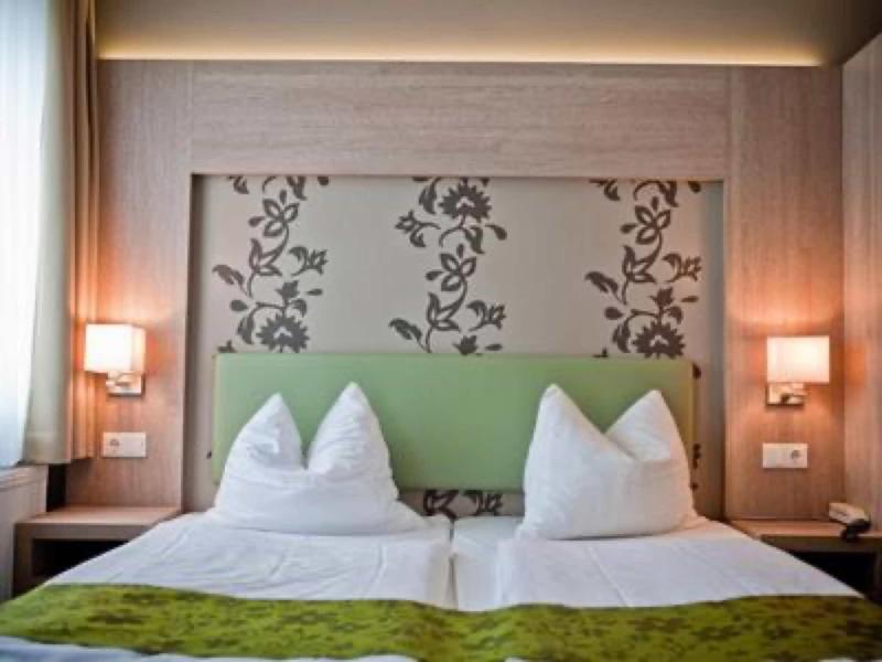 Ein modernes Schlafzimmer mit zwei Einzelbetten, grünem Kopfteil und floralem Wandmuster.