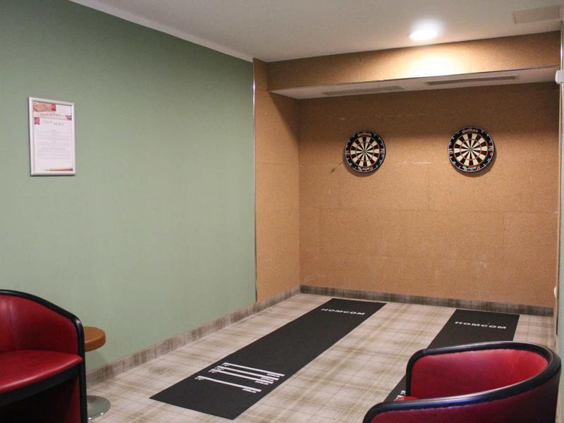Indoor-Dartbereich mit zwei Dartscheiben an der Wand, Teppichbahnen und roten Ledersesseln.