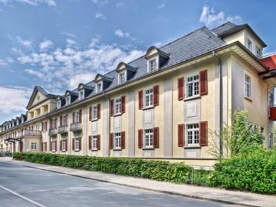 Langes, historisches Hotelgebäude mit mehreren Gauben und roten Fensterläden bei sonnigem Wetter.
