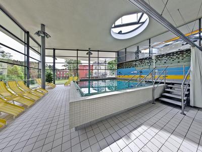 Moderner Innenpool mit großen Fensterfronten, gelben Liegestühlen und hellem Fliesenboden.