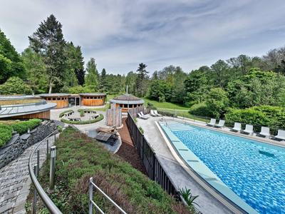 Large outdoor pool with loungers surrounded by trees and a terrace with seating.