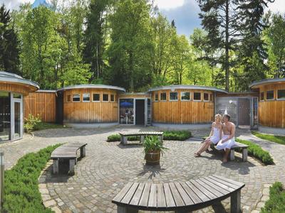 Round wooden bungalows in a green forest setting with seating in the foreground.