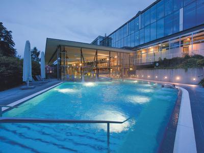 Illuminated outdoor pool at dusk beside modern hotel building with glass facade.
