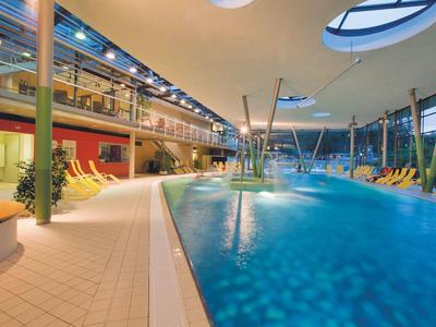Modern indoor pool with blue water, lounge chairs, and plenty of natural light.