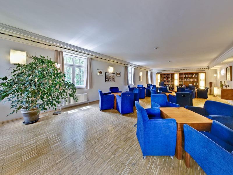 Bright lounge with blue armchairs, wooden tables, large window and plants