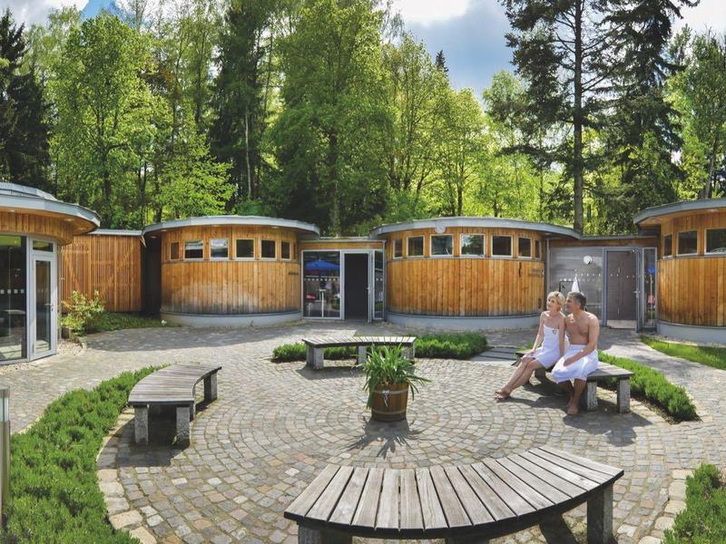 Round wooden bungalows in a green forest setting with seating in the foreground.
