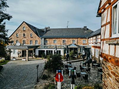 Großes Fachwerkhaus mit steinernem Haupthaus, Terrasse und gepflastertem Hof unter bewölktem Himmel.