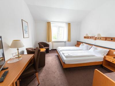 Bright hotel room with double bed, desk, chair, and window with yellow curtains.