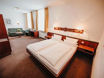 Spacious hotel room with double bed, seating area, and warm wooden furniture.