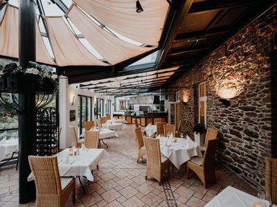 Überdachte Terrasse eines Restaurants mit gedeckten Tischen und Stühlen aus Korbgeflecht.