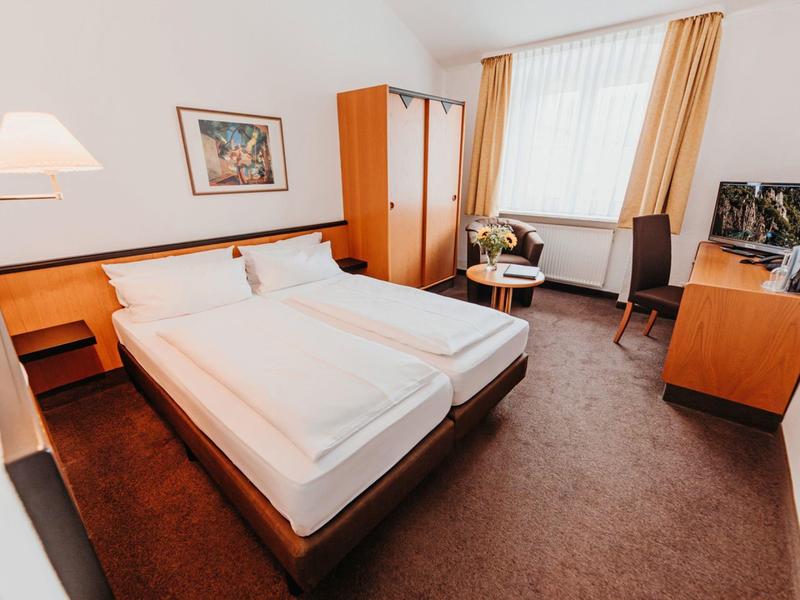 Bright hotel room with double bed, table, chairs, wardrobe, and television.