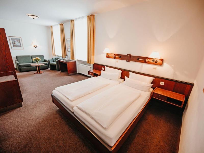 Spacious hotel room with double bed, seating area, and warm wooden furniture.