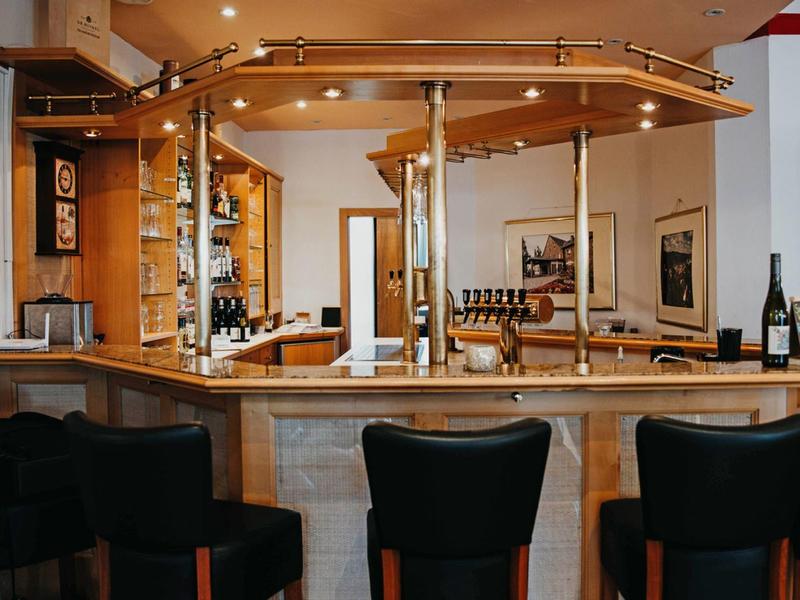 Cozy hotel bar with wooden counter, black stools, and mirrors.