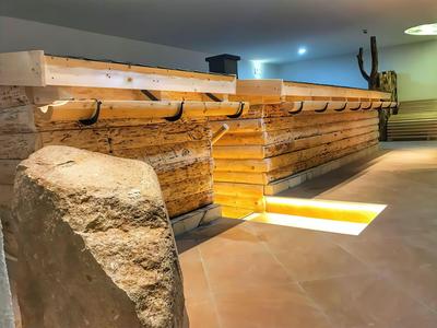 Innenraum mit moderner Holztheke, beleuchtetem Boden und Steinmauer im Hintergrund