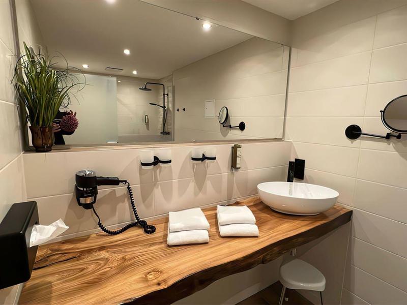 Modern bathroom with wooden counter, large mirror, sink, and white towels.