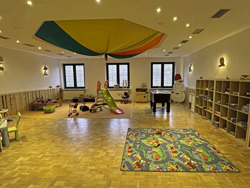 Bright playroom with colorful rug, slide, seating, and large colorful hanging element.