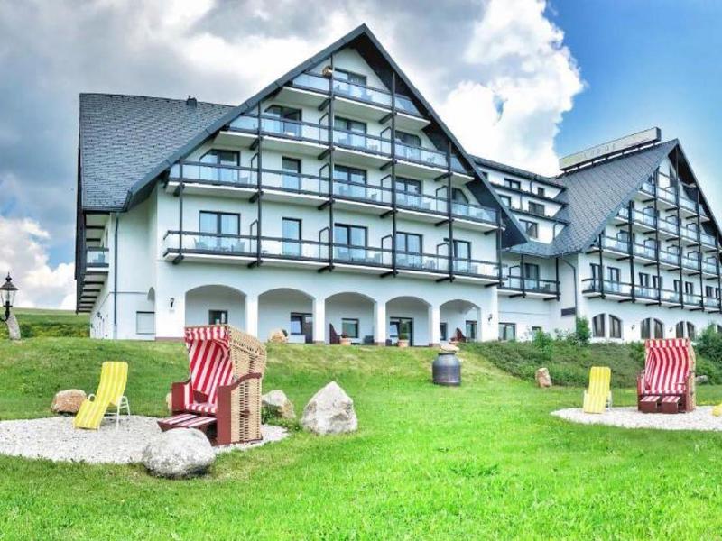 Large half-timbered hotel with manicured lawn and colorful deck chairs in foreground.