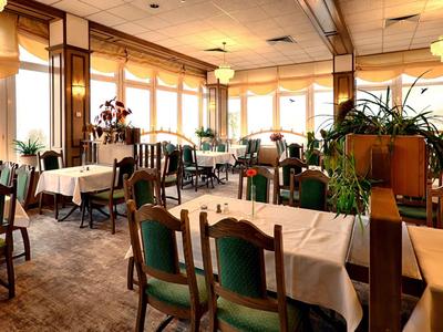 Gemütlicher, hell beleuchteter Speisesaal mit großen Fenstern, grünen Stühlen und weißen Tischdecken.