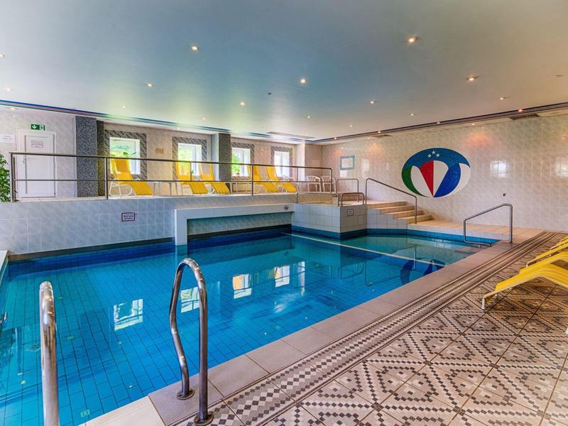 Moderní vnitřní bazén s čistou modrou vodou, lehátky a dekorativní stěnou v hotelu.