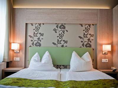 Modernes Hotelzimmer mit zwei Einzelbetten und dekorativem grünen Kopfteil vor gemustertem Hintergrund.