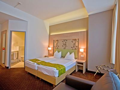 Gemütliches Hotelzimmer mit komfortablem Bett, zwei Nachttischen und braunem Teppichboden.