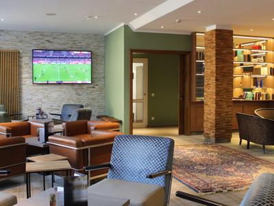 Gemütlicher Hotel-Loungebereich mit Ledersesseln, Teppichboden und Fernseher an der Wand.