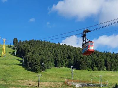 Eine Seilbahn fährt über eine grüne Berglandschaft mit Bäumen und klarem Himmel.