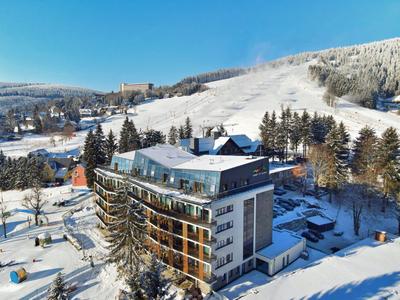 Mehrstöckiges Hotel im verschneiten Skigebiet mit sonnenbeschienenen Hängen und blauen Himmel.