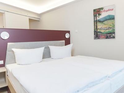 Hell eingerichtetes Hotelzimmer mit Doppelbett und modernem Kopfteil.