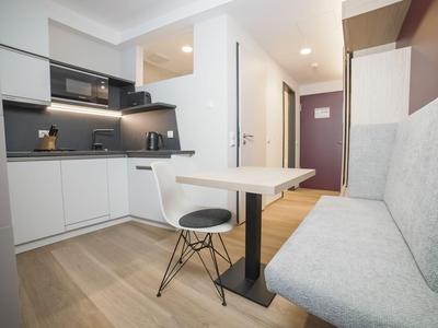 Kleine moderne Küche mit Esstisch, weißem Stuhl und grauer Sitzbank in einer Wohnung.