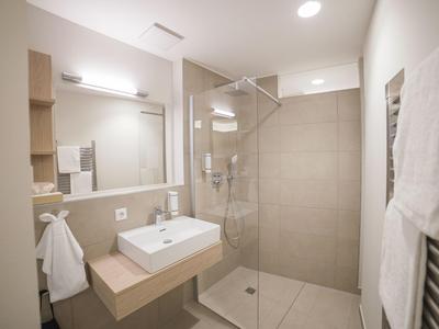 Moderner Badezimmerbereich mit Waschbecken, Spiegel und begehbarer Dusche in neutralen Farben.