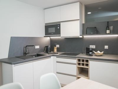 Moderne Küchenecke mit grauen Arbeitsflächen, weißen Schränken und eingebauter Mikrowelle.