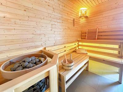 Helle Sauna mit Holzbänken, Saunaofen mit Steinen und Holzeimer mit Kelle.