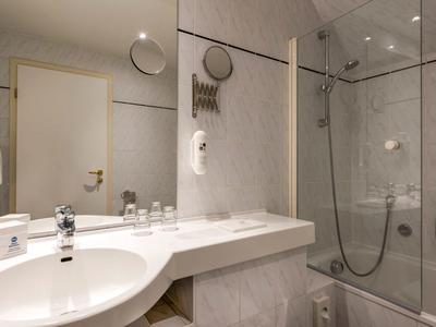 Bright bathroom with sink, mirror, hairdryer, and bathtub with shower fixture.