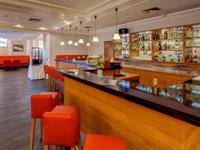 Modern hotel bar area with wooden counter, red bar stools, and comfortable seating.