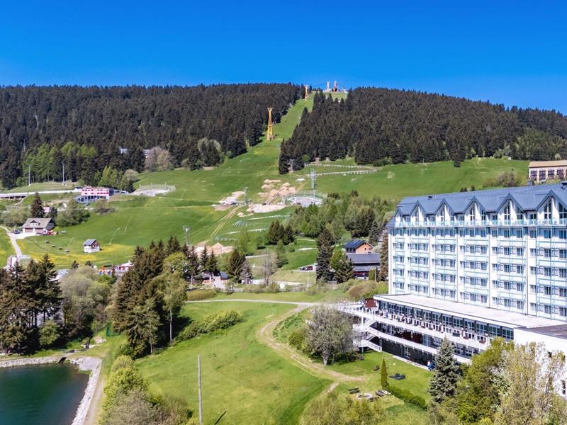 Hotel in front of forested hill with green meadows and blue sky