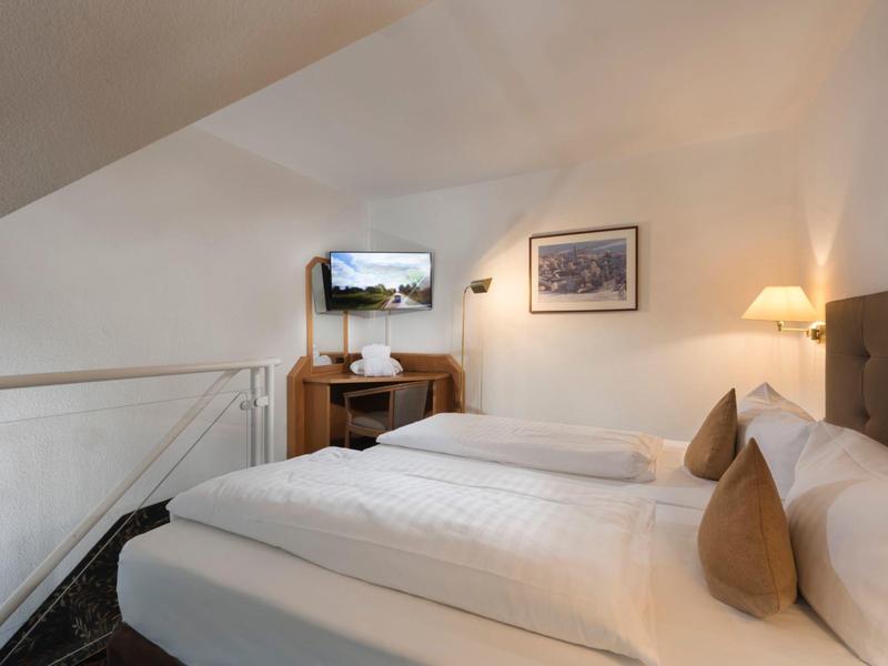 Bright bedroom with slanted ceiling, double bed, TV, and wooden furniture in a hotel room.