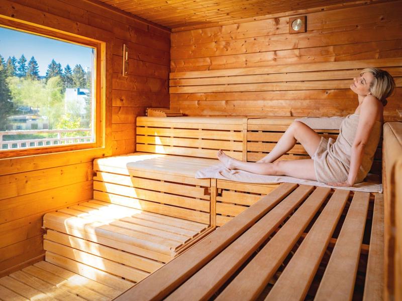 Woman relaxing inside a wooden sauna cabin with a view of trees.