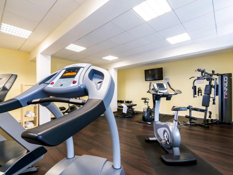 Modern gym room with various exercise machines and wooden flooring.