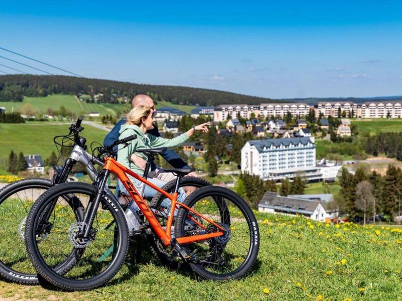 Child with bike on a meadow overlooking a hotel and houses in the background.