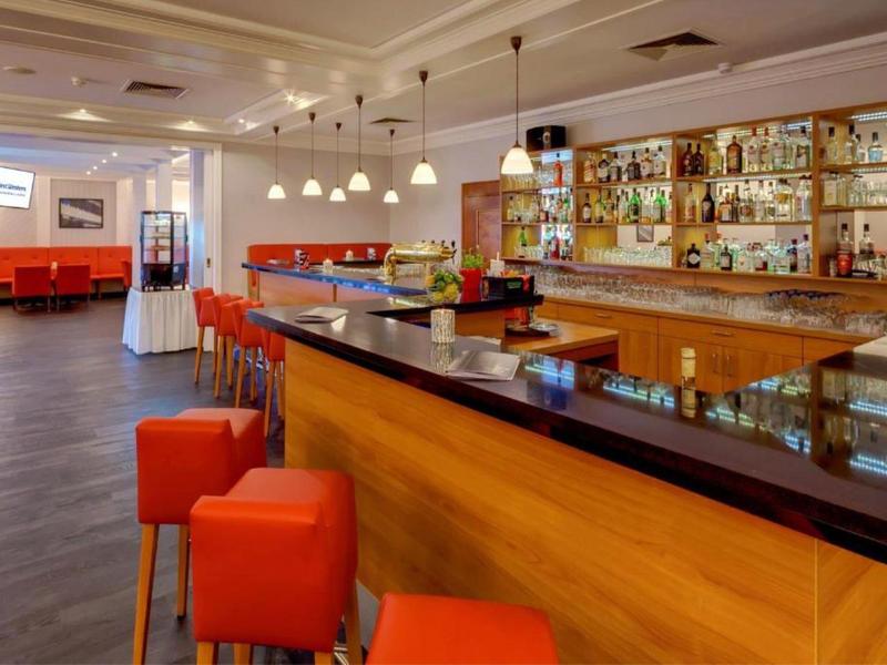 Modern hotel bar area with wooden counter, red bar stools, and comfortable seating.