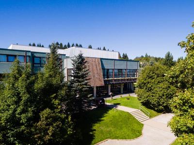 Modernes Hotelgebäude mit großen Fenstern, umgeben von grünen Bäumen und einem gepflasterten Weg.