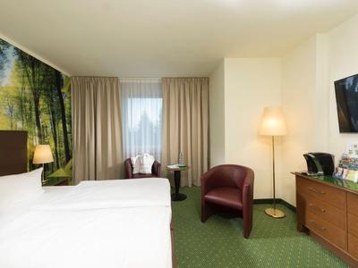 Moderne hotelkamer met tweepersoonsbed, fauteuils, tv en groen tapijt.