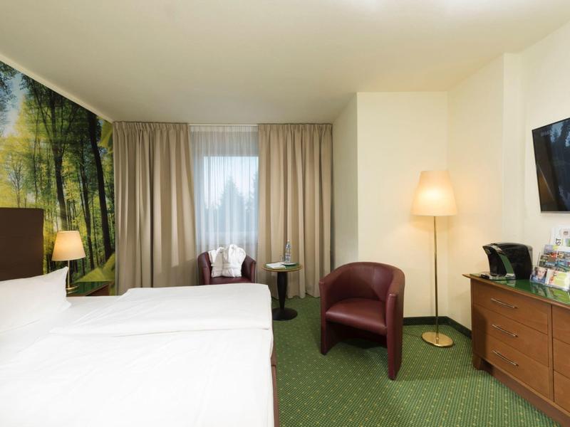 Hotelzimmer mit Doppelbett, grüner Teppichboden, rotem Sessel und Naturwandbild.